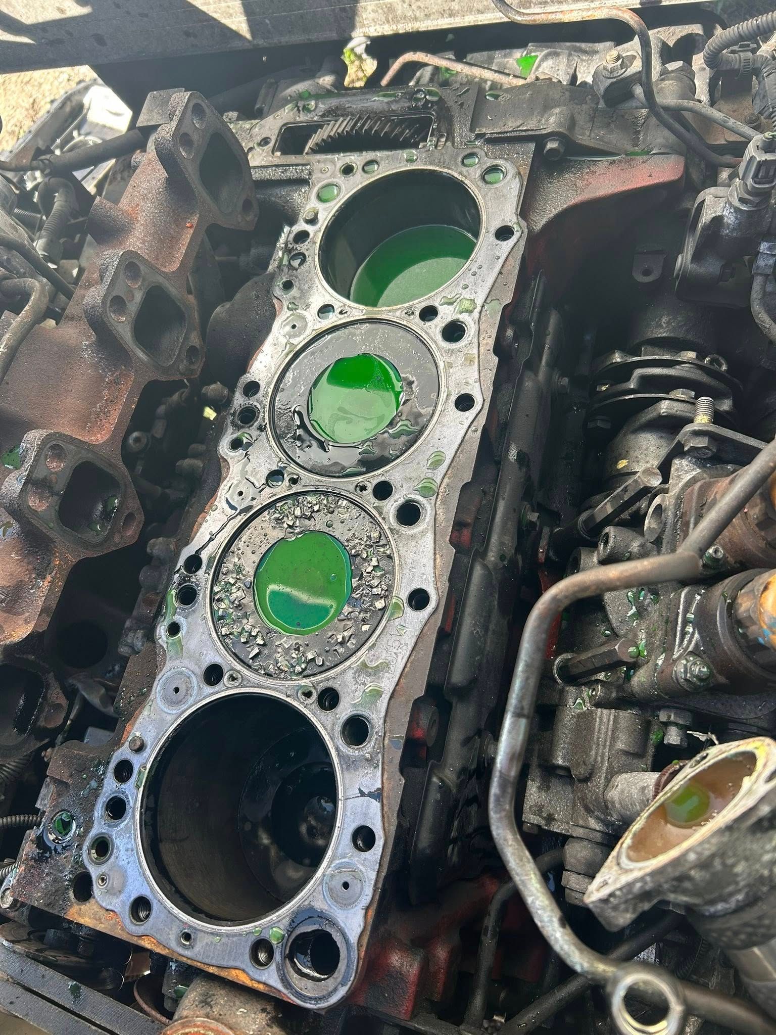 Engine block with three cylinders visible, filled with green liquid, in a scrapyard setting.