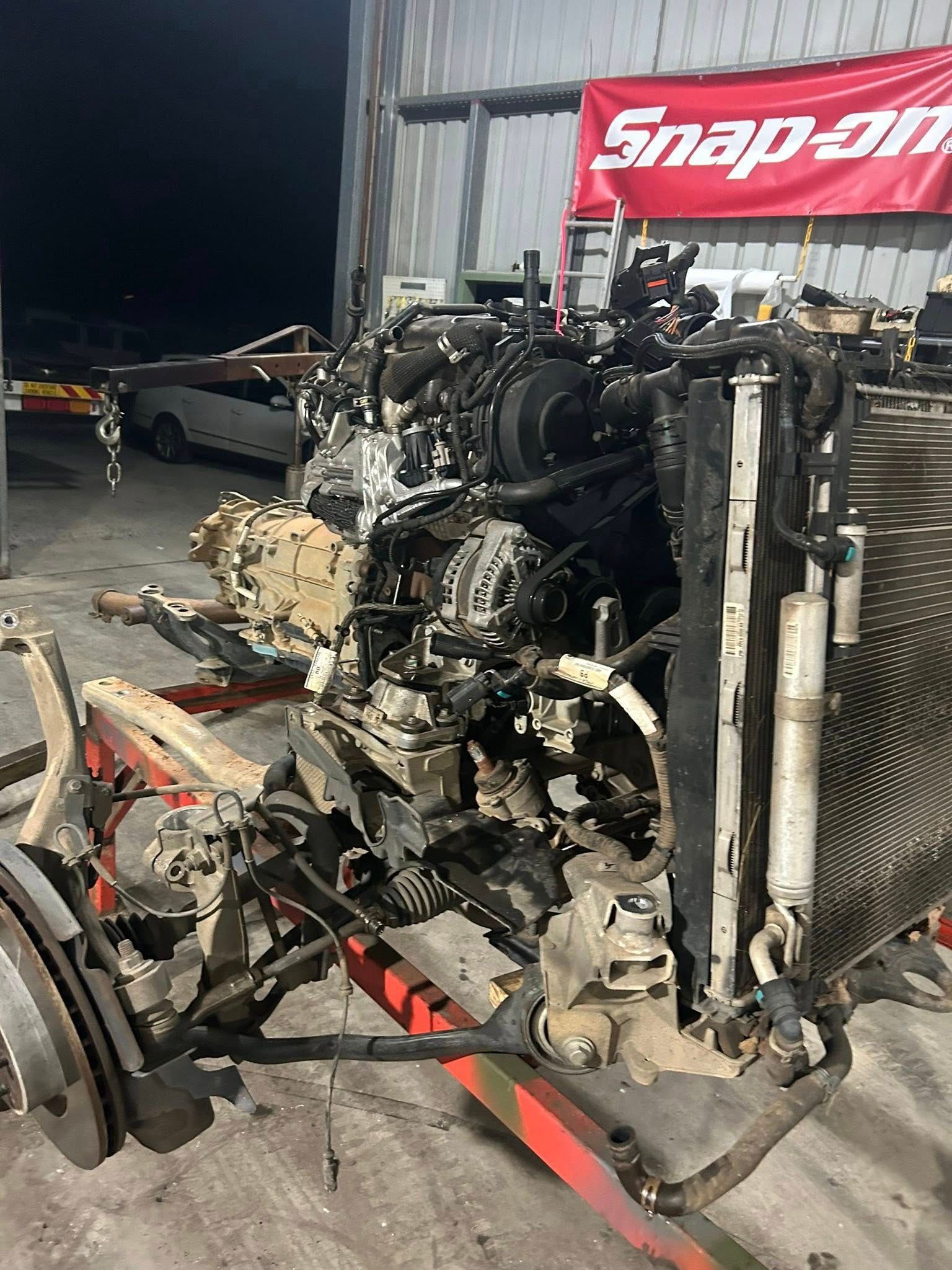 Car engine and components on a red stand inside a shop, radiator visible. Snap-on sign in the background.