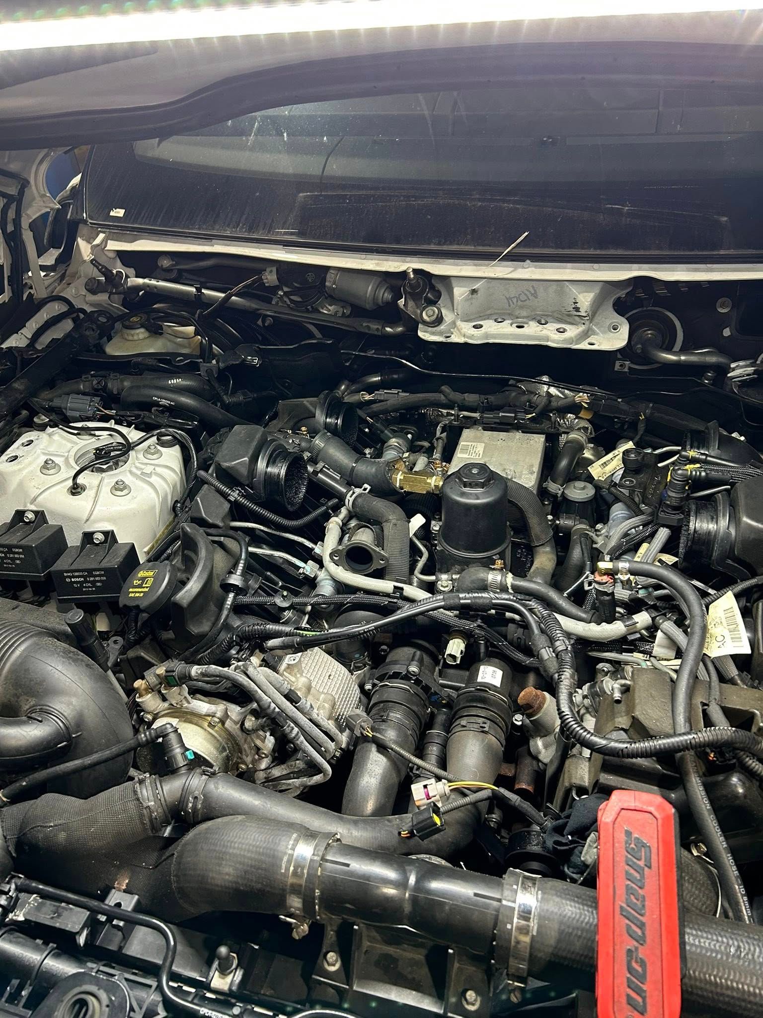 Engine bay of a vehicle, filled with black components and wiring. A Snap-on tool is visible on the right.