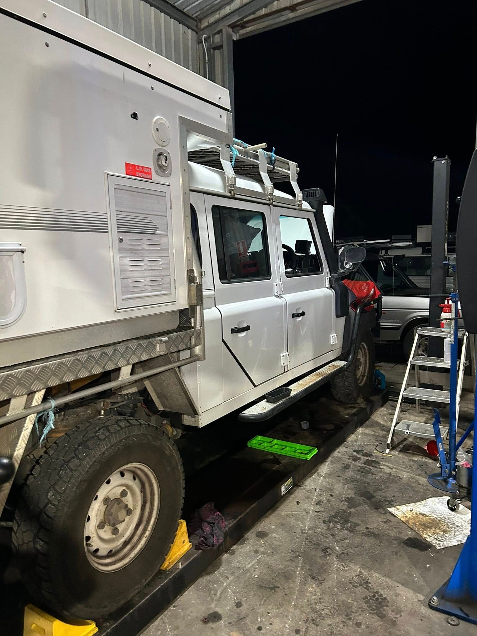 Silver off-road vehicle with camper top inside a garage. Includes roof rack, side steps, and large tires.
