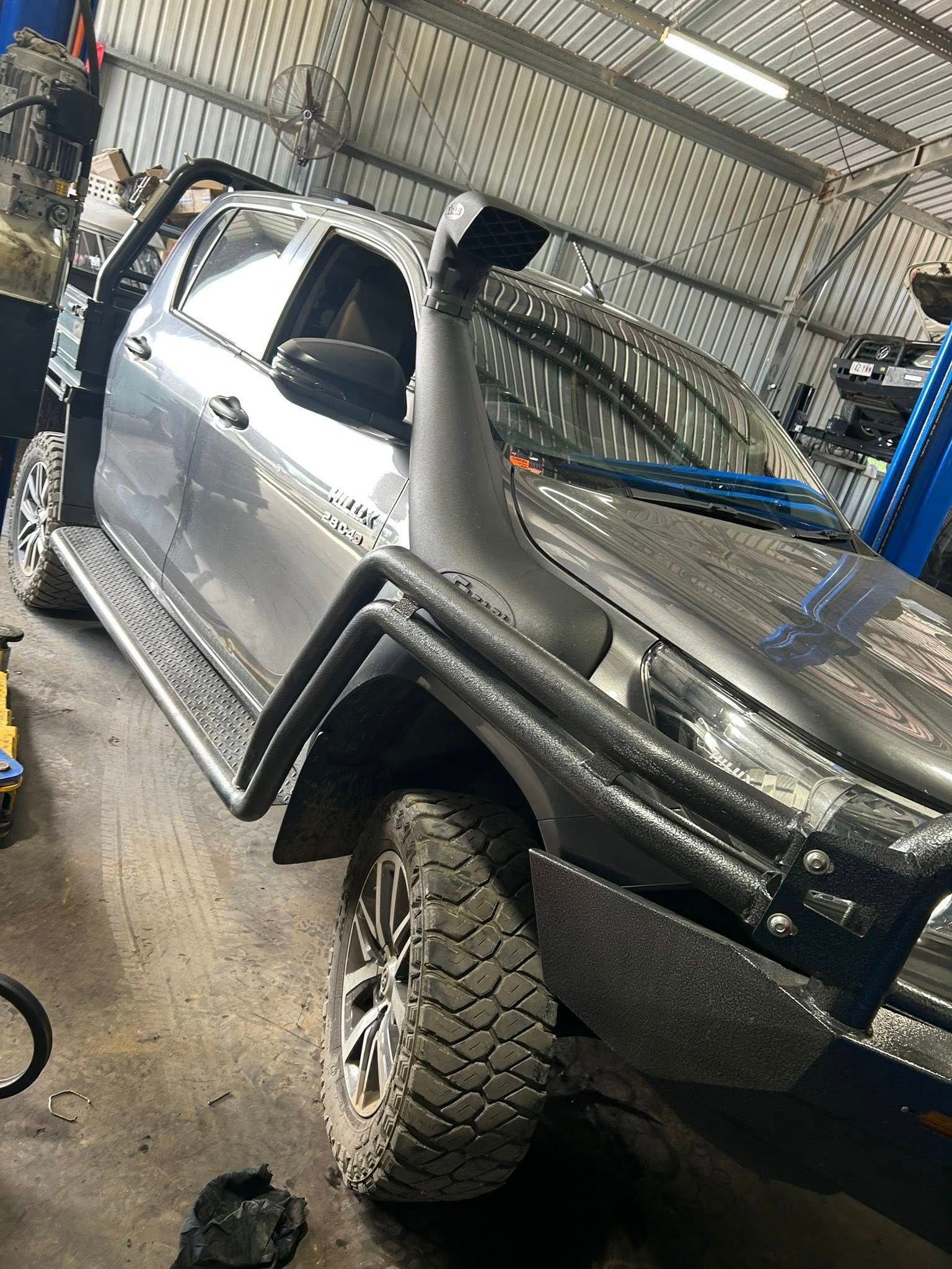 Gray pickup truck with a snorkel and off-road tires inside a garage.