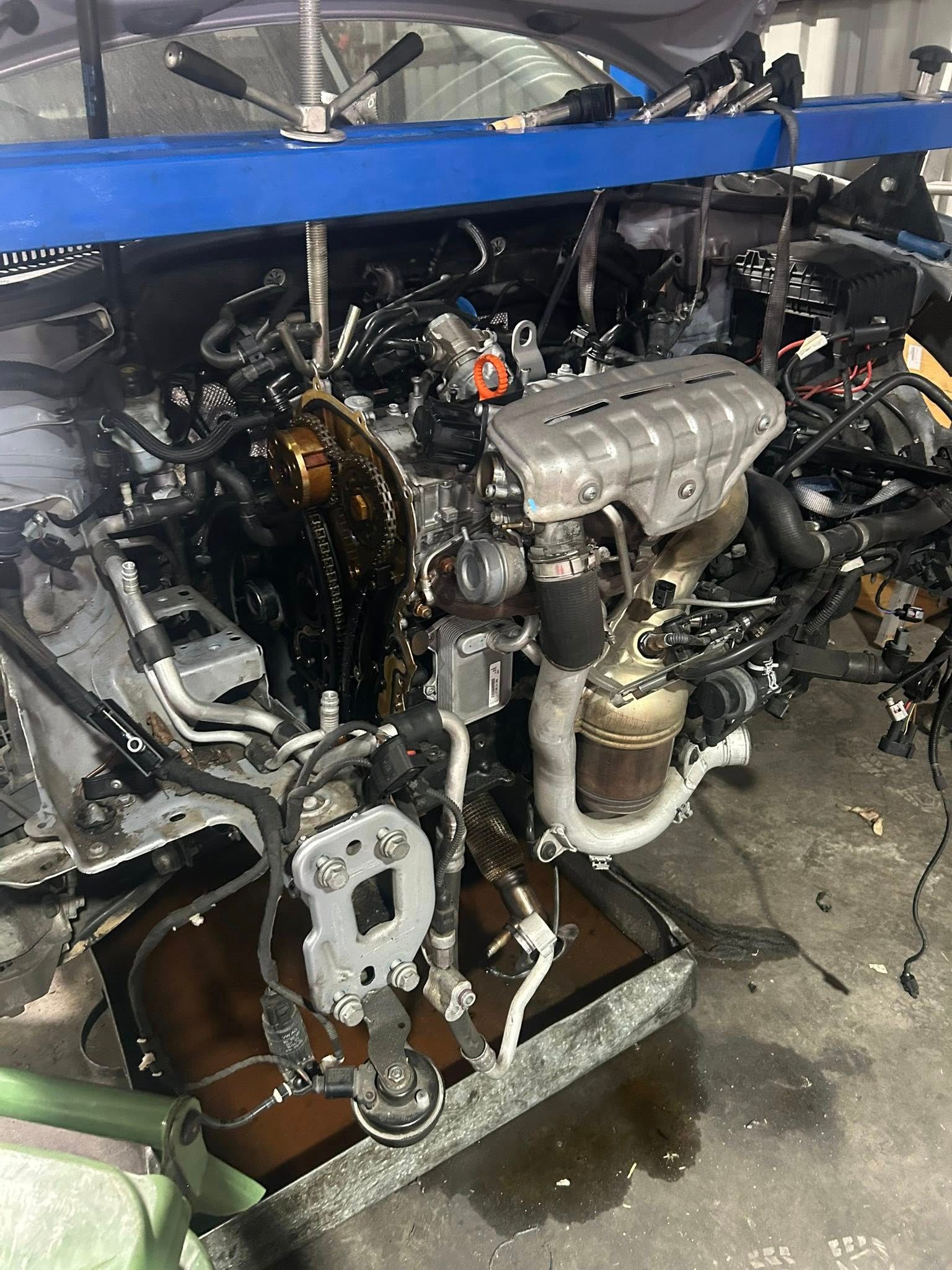 Car engine, complex assembly of components, oily, in a repair setting.