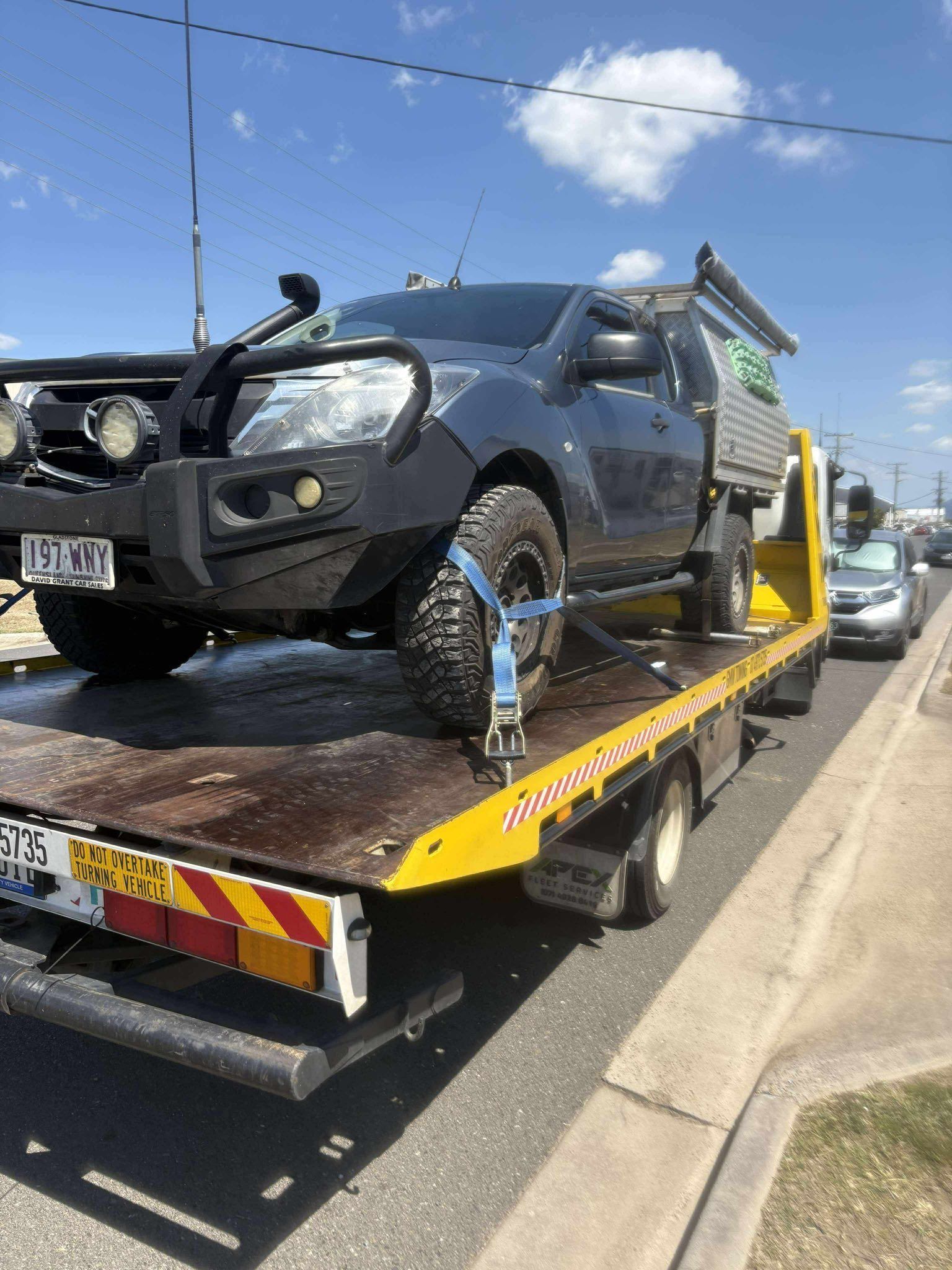 A dark pickup truck is secured on a yellow tow truck on a city street.