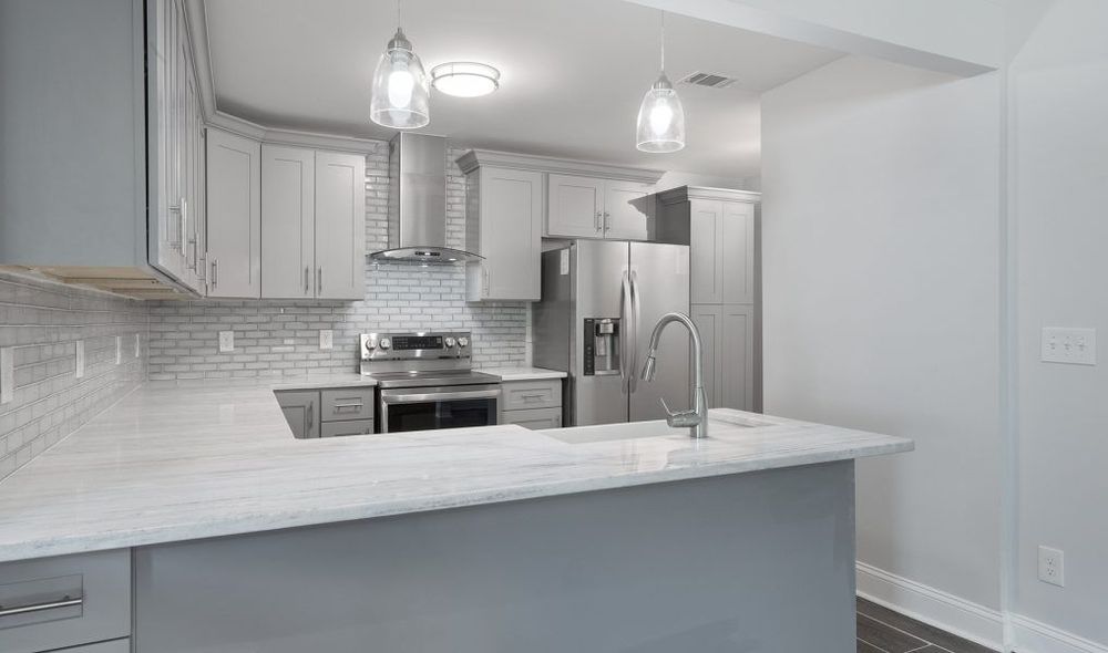 Modern kitchen with gray cabinets, stainless steel appliances, and white countertops.