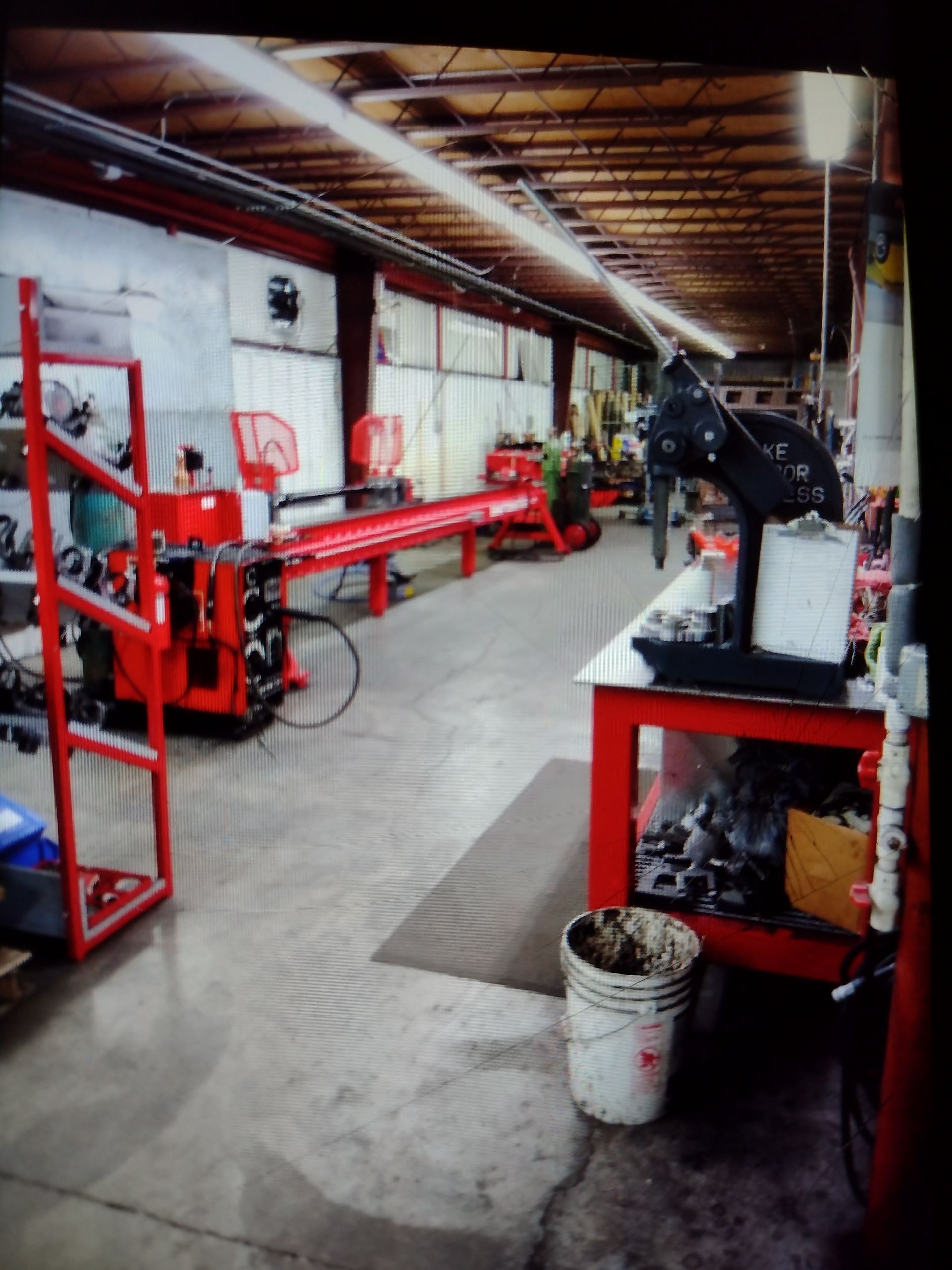 An industrial workshop floor featuring a long, red metalworking machine and a black press on a red workstation.