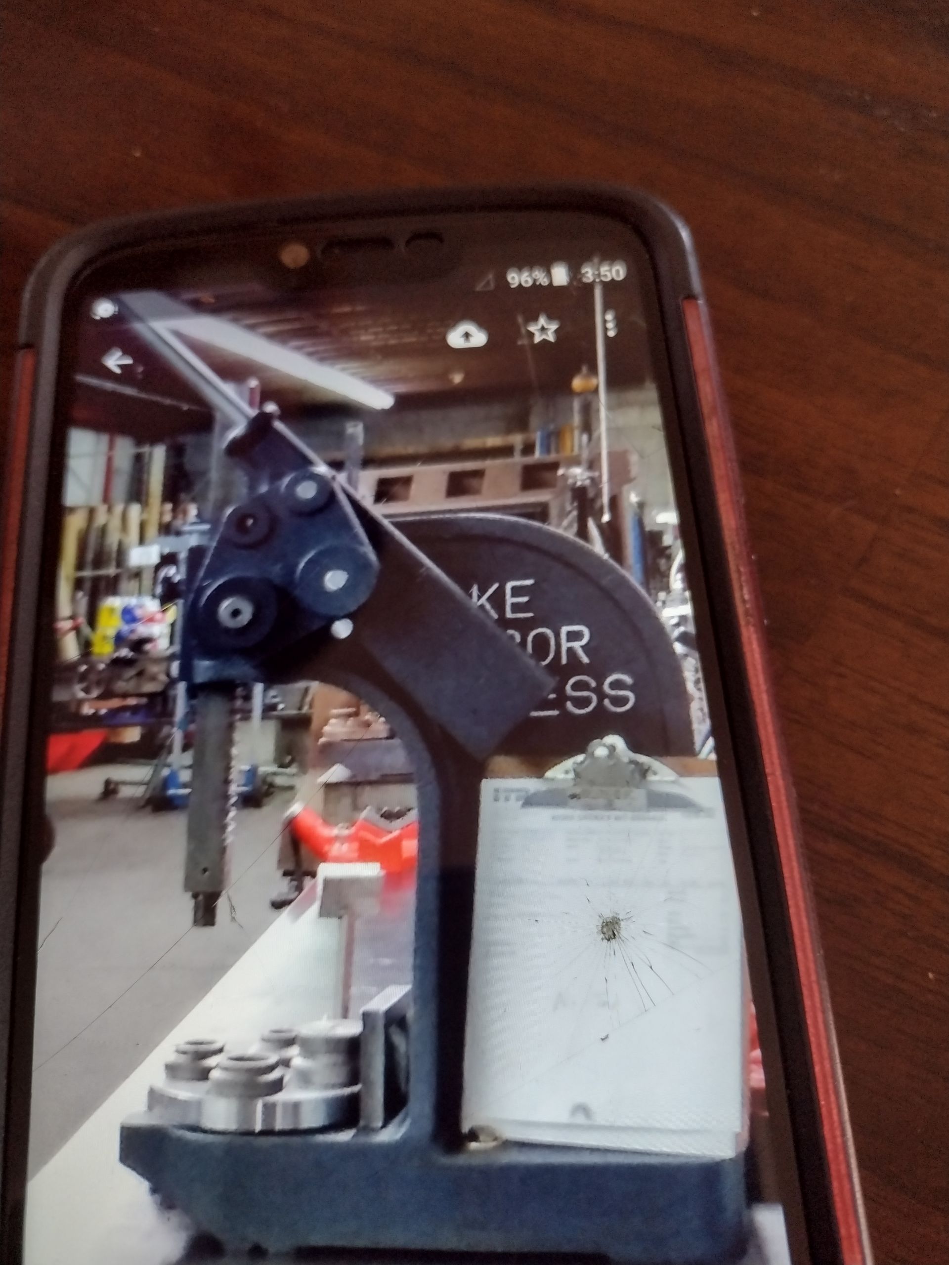 A blue manual arbor press sits on a table, shown on a smartphone screen against a workshop background.