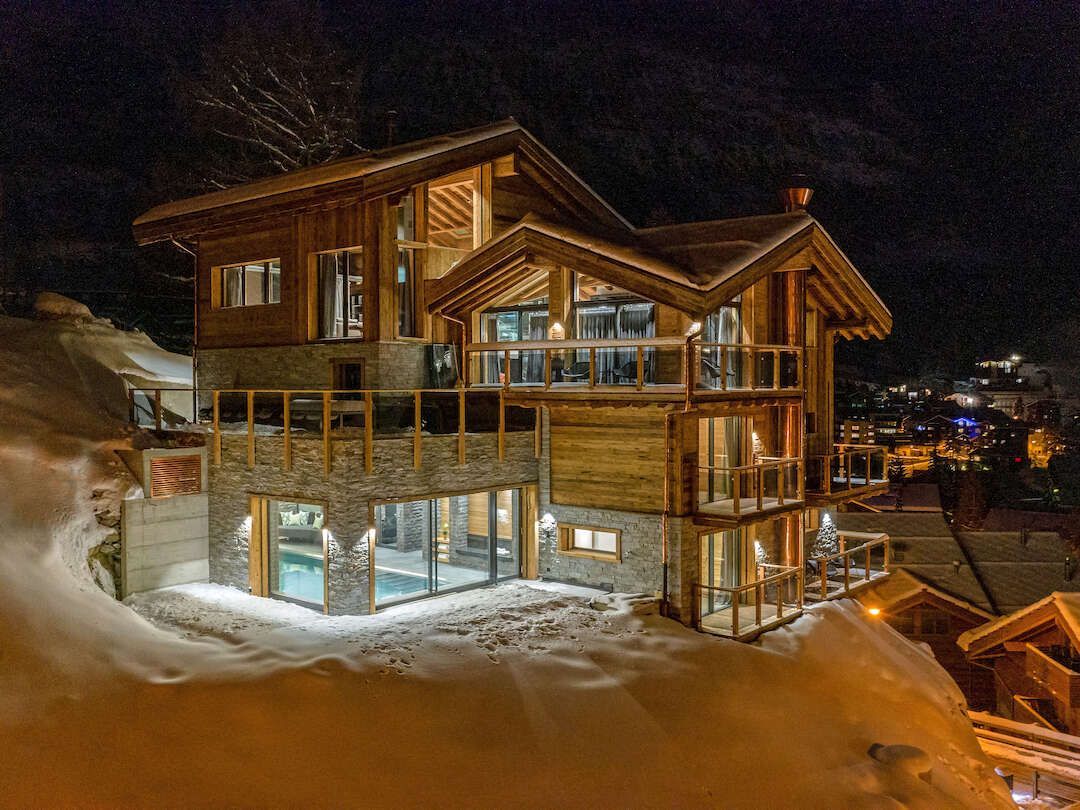 A large wooden house is surrounded by snow at night.