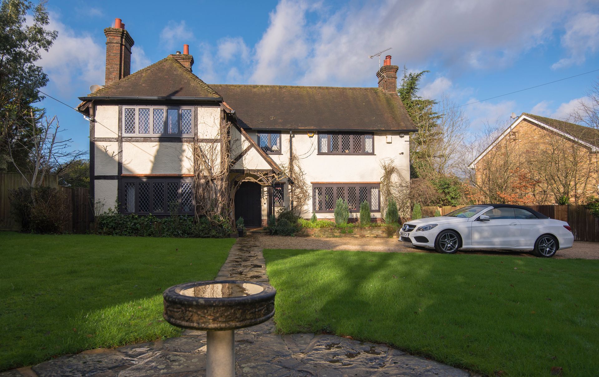 A white car is parked in front of a large house.