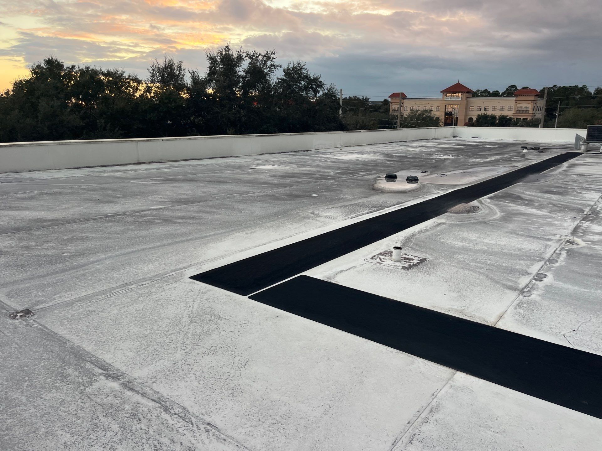 White commercial flat roof with skylights and an open vent against a sunny blue sky.