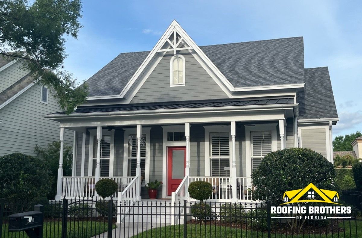 A gray house with a red door, white porch, and a dark gray roof.
