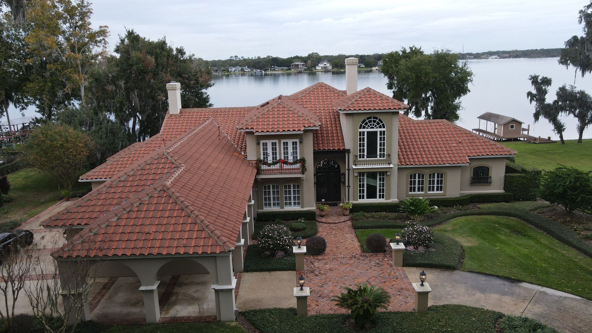 Roofer using a nail gun to install asphalt shingles on a roof; hammer and tool belt nearby.
