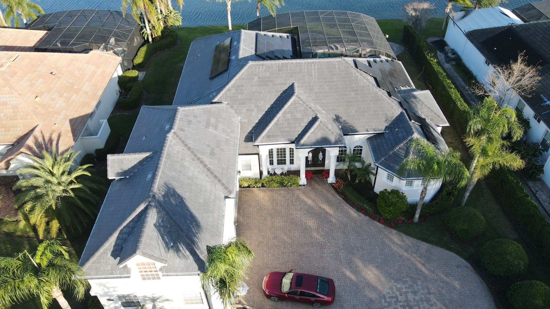 Two workers on ladders repairing the roof of a house with gray siding under a cloudy sky.