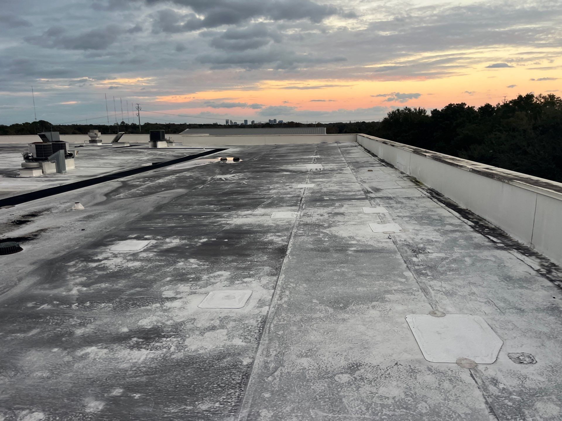 White commercial building with flat roof and HVAC units, set against a backdrop of trees and a blue sky.