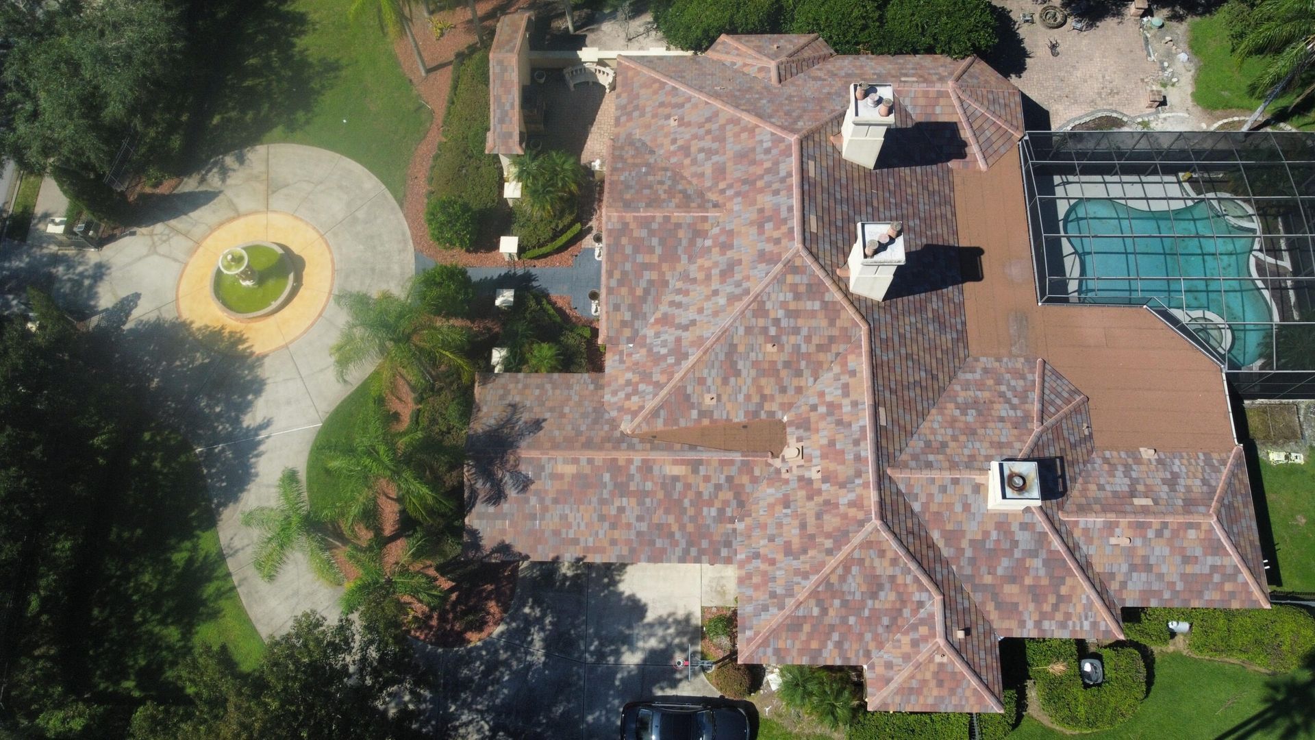 Aerial view of a large house with a brown tiled roof, pool, and circular driveway.