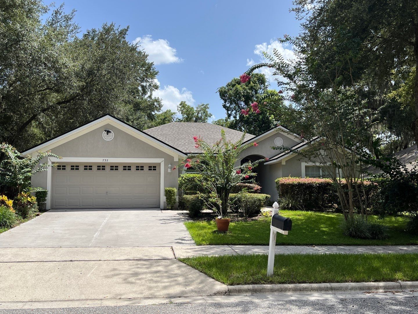 Tan house with a two-car garage, gray roof, and manicured lawn on a sunny day.