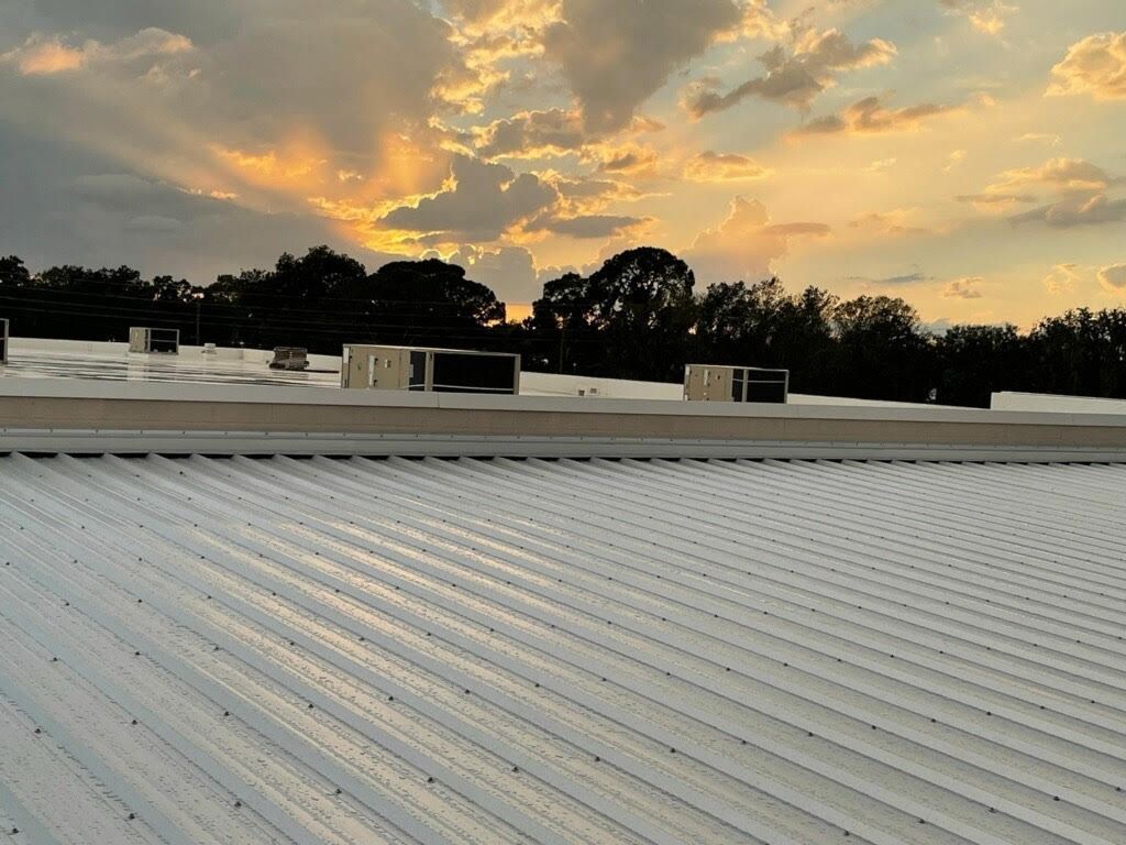 White corrugated roof with rooftop units, sunset with golden clouds above trees.