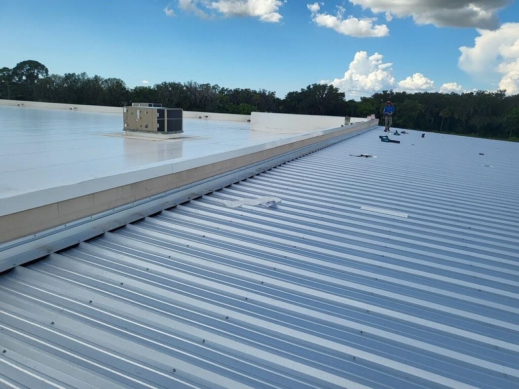 View of a corrugated metal roof with a white coating, a person, and blue sky with clouds.