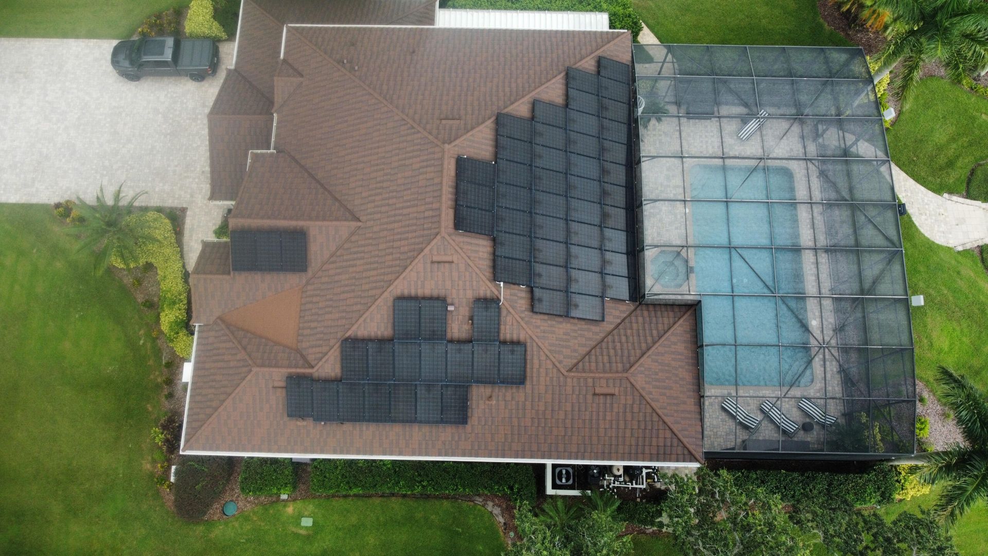 Aerial view of a house with solar panels on the brown roof, a pool covered by glass, and green lawn.