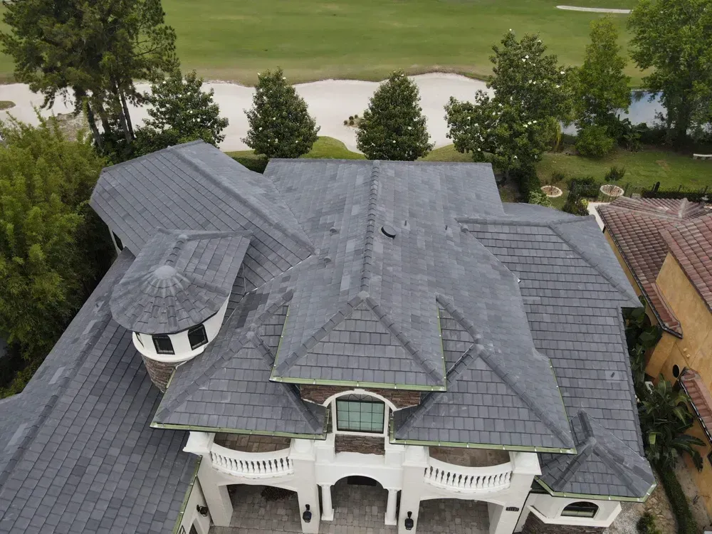 Aerial view of a luxury home with gray roof, white balcony, and green lawn in the background.