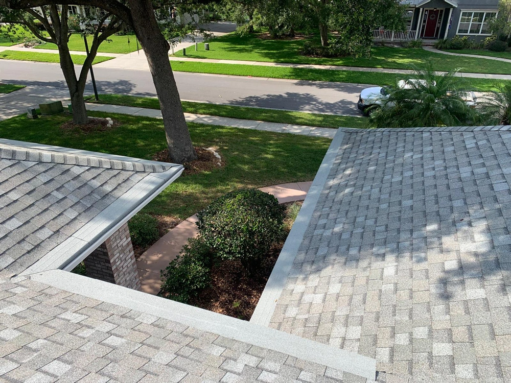 View from rooftop of shingled roof overlooking a street, yard with tree, and shrubbery.