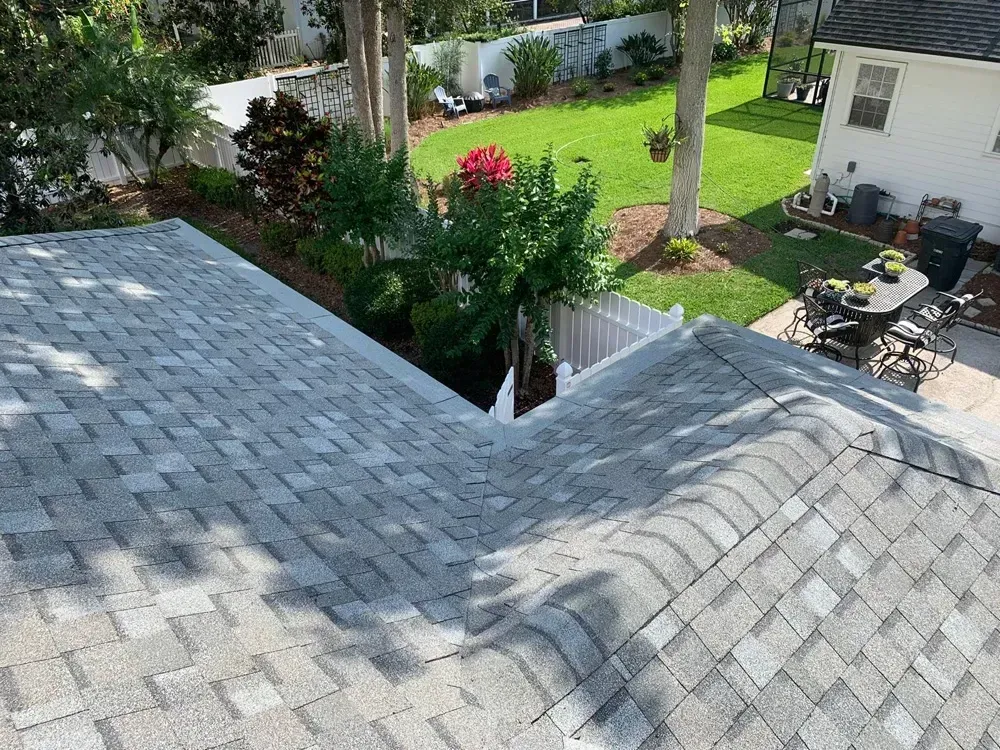 Overhead view of a gray shingled roof with trees and backyard in the background.
