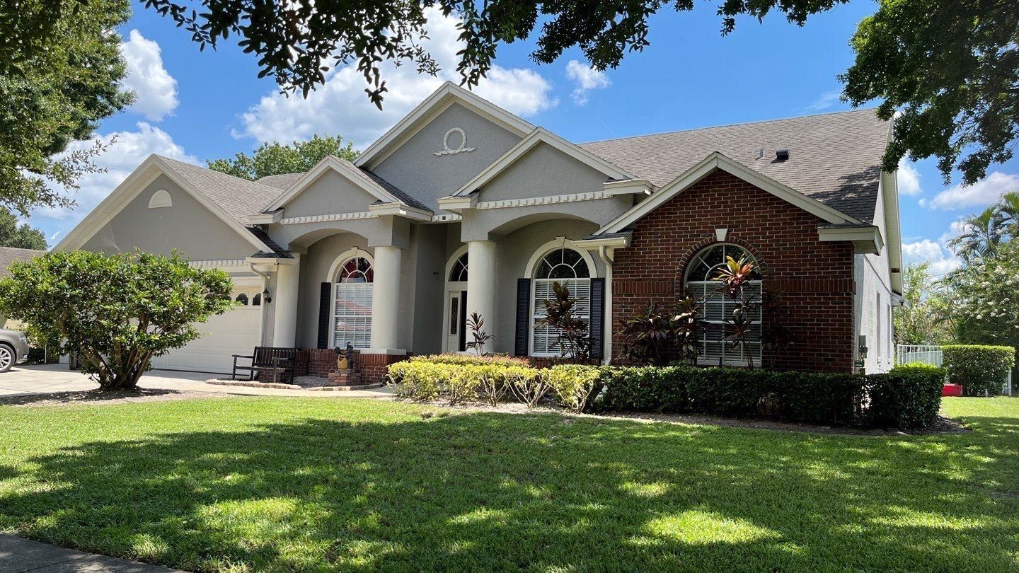 House with gray siding, brick accents, arched windows, and a green lawn under a blue sky.