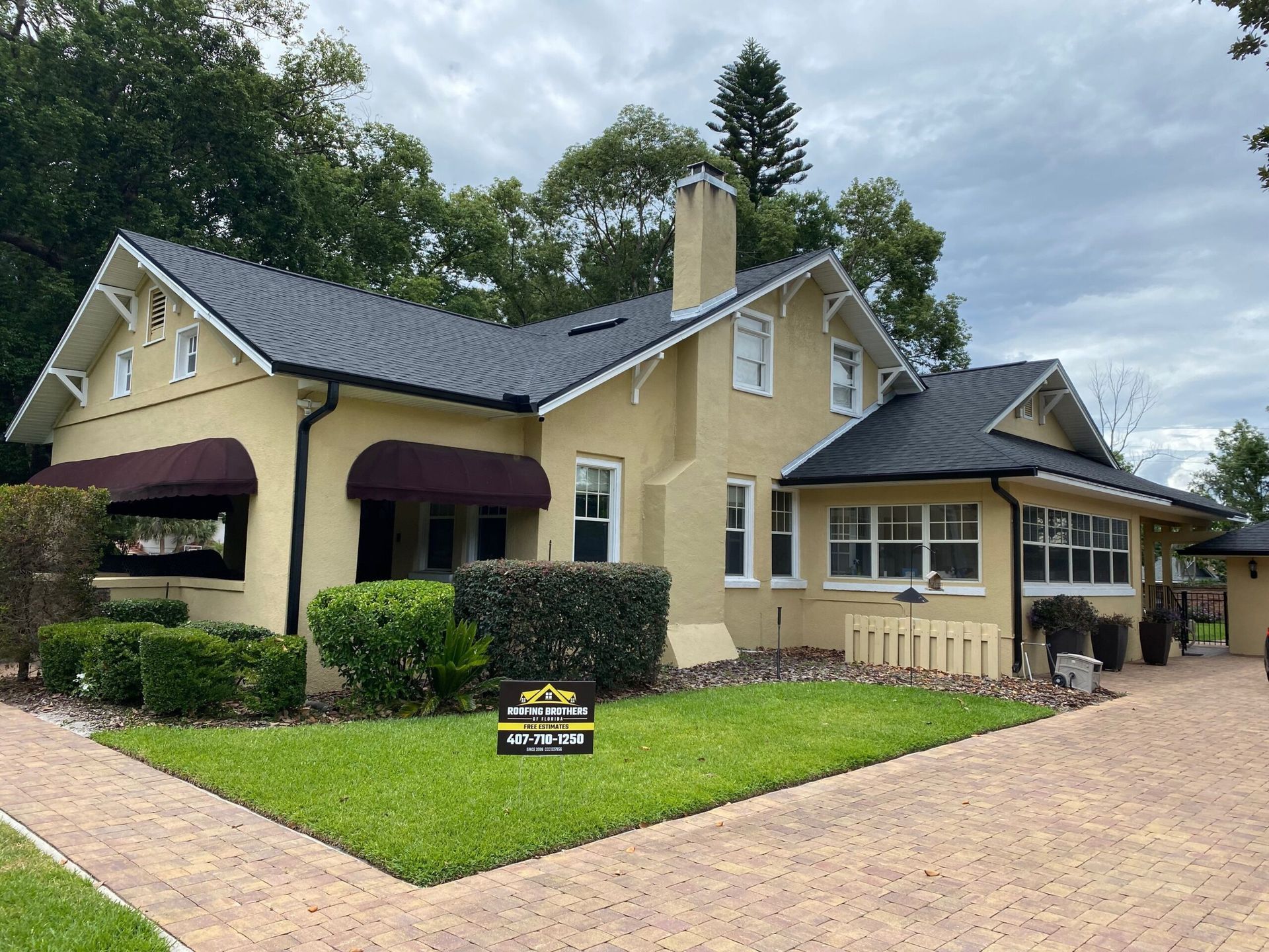Yellow house with a dark roof and a maroon awning, set against a cloudy sky.