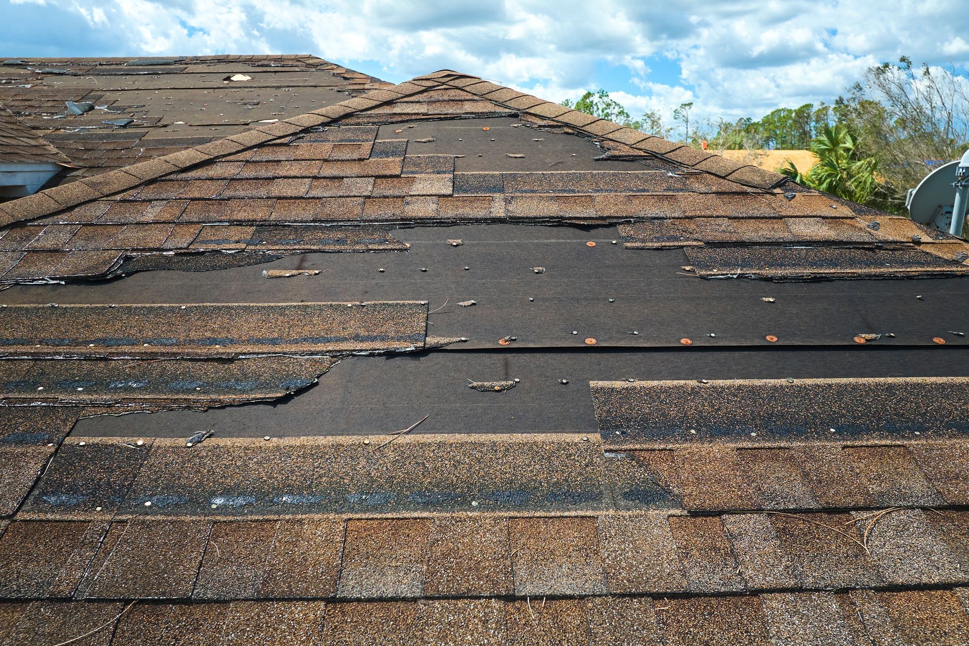 Damaged asphalt shingle roof, missing shingles exposing black underlayment; overcast sky.