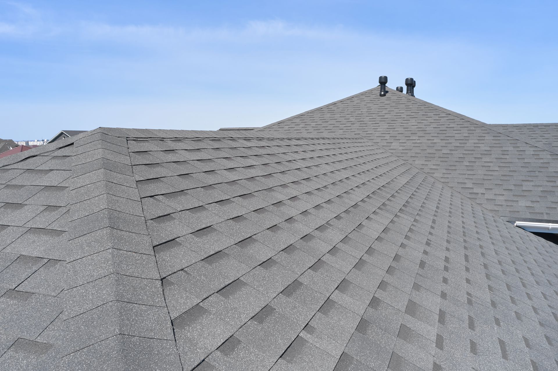 Gray shingled roof under a clear blue sky. Chimney and vents are visible.