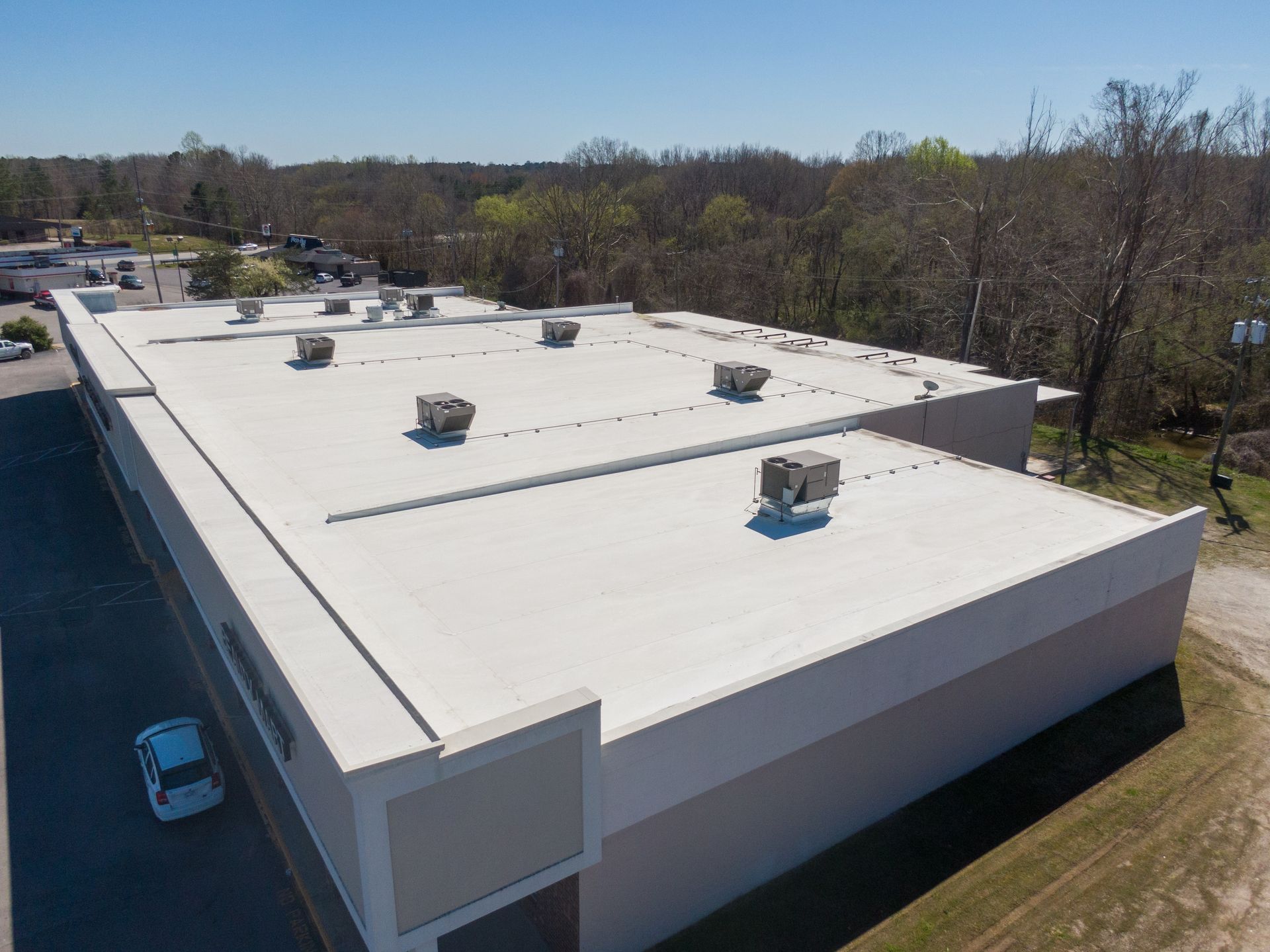 White commercial building with flat roof and HVAC units, set against a backdrop of trees and a blue sky.