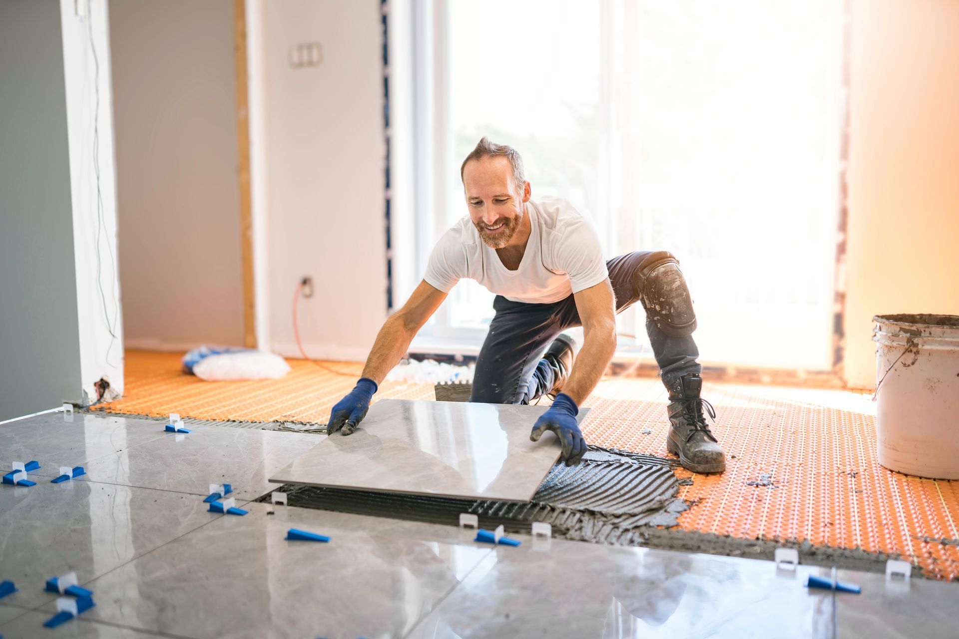 A man is laying a tile floor in a room.