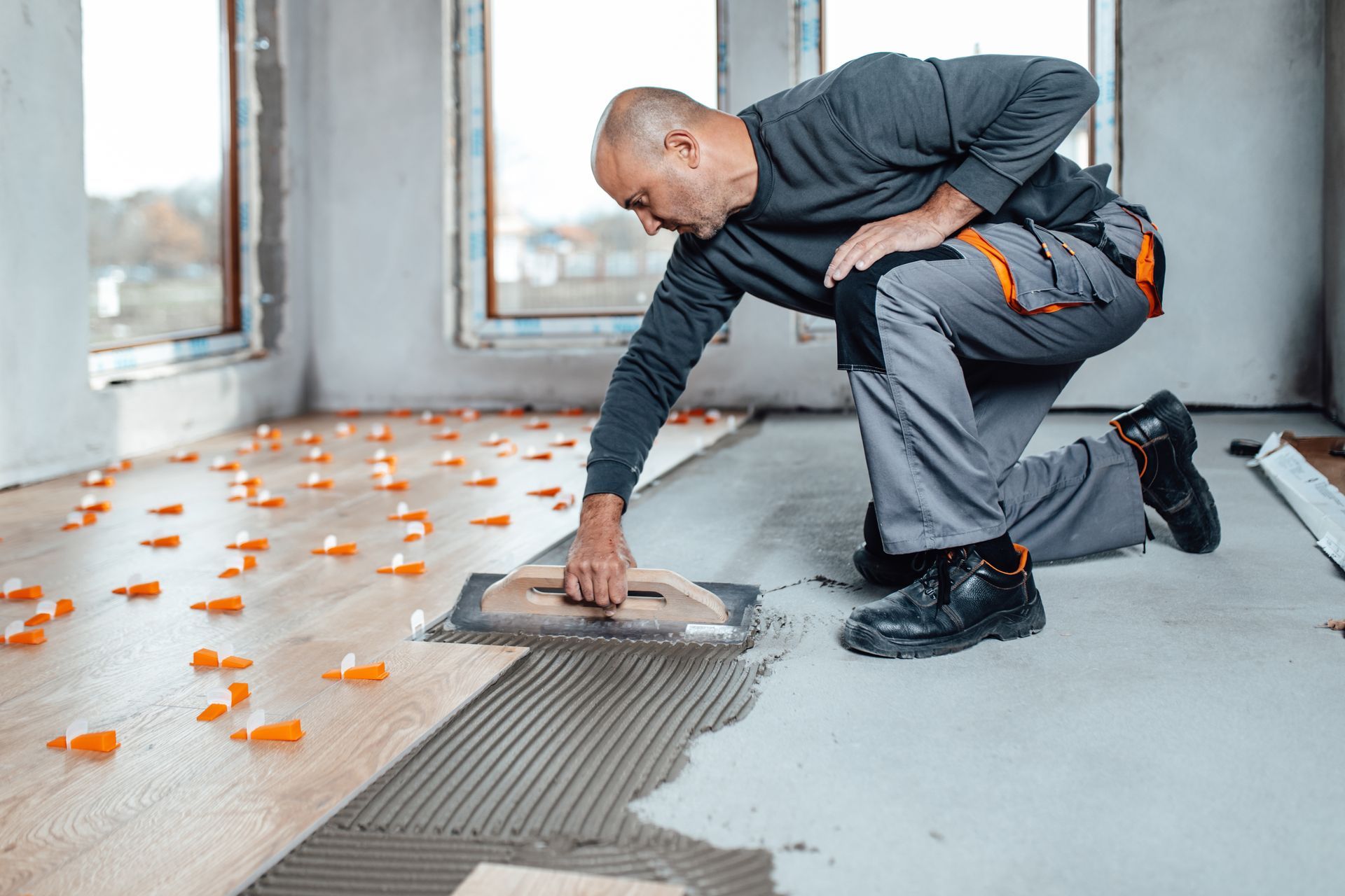A man is kneeling down and applying tile to a wooden floor.