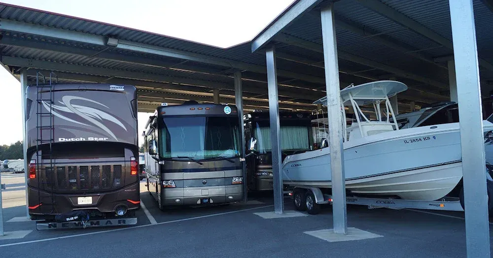 RV and boat under a metal roof, parked side-by-side in a storage facility.