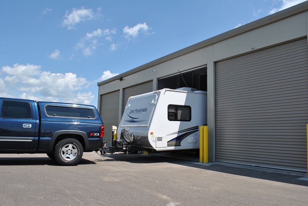 Blue truck towing a white RV into a storage unit with a large, open garage door.