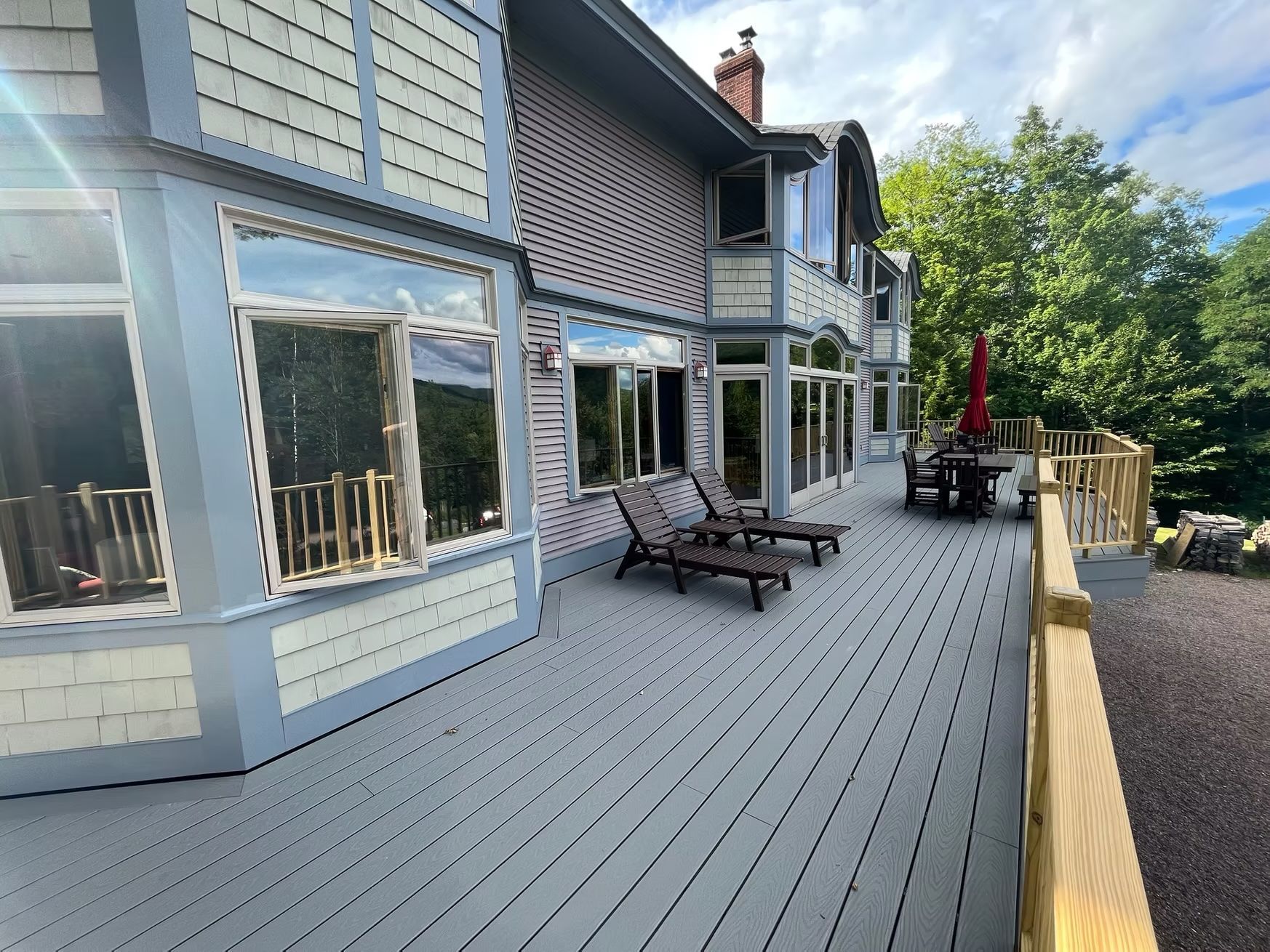 A large house with a large deck with chairs and tables on it.