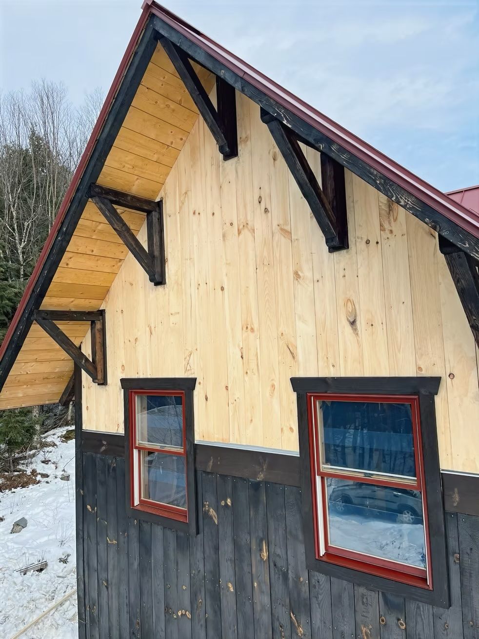 A wooden house with a red roof and two windows