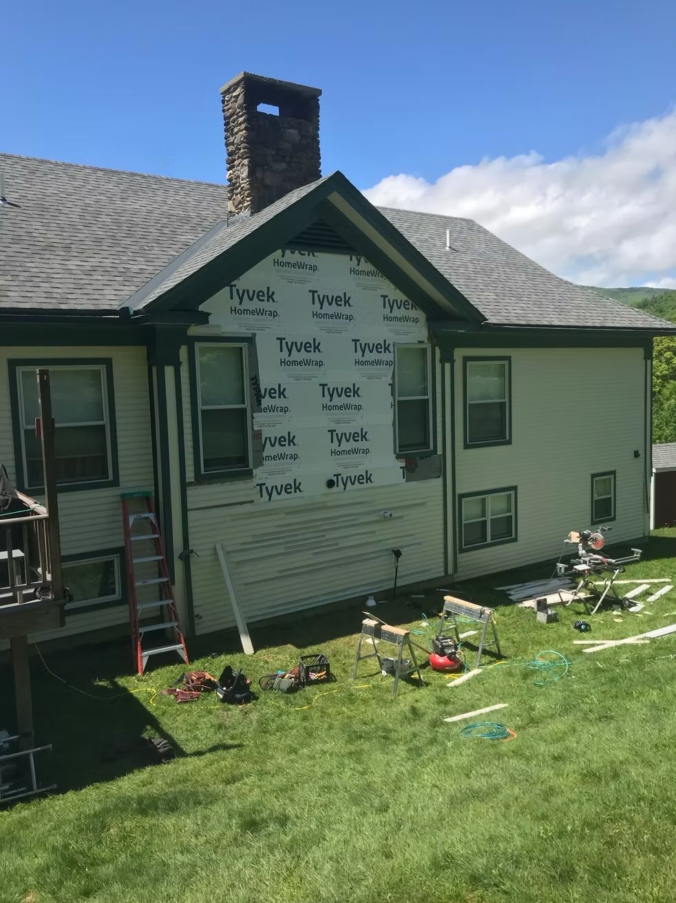 A large white house is being remodeled with a ladder in the backyard.