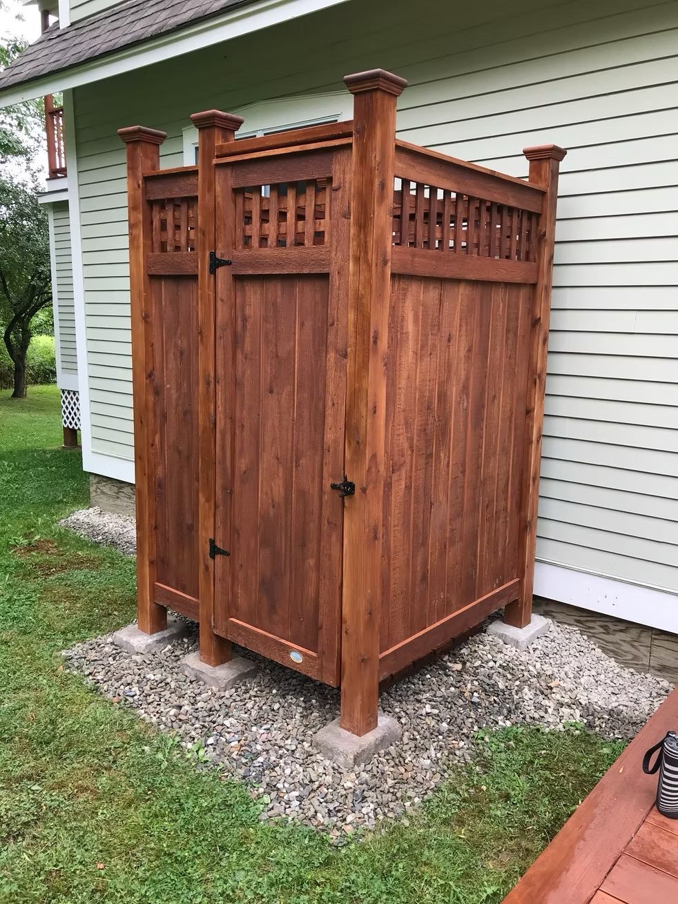 A wooden shower stall is sitting in the grass in front of a house.