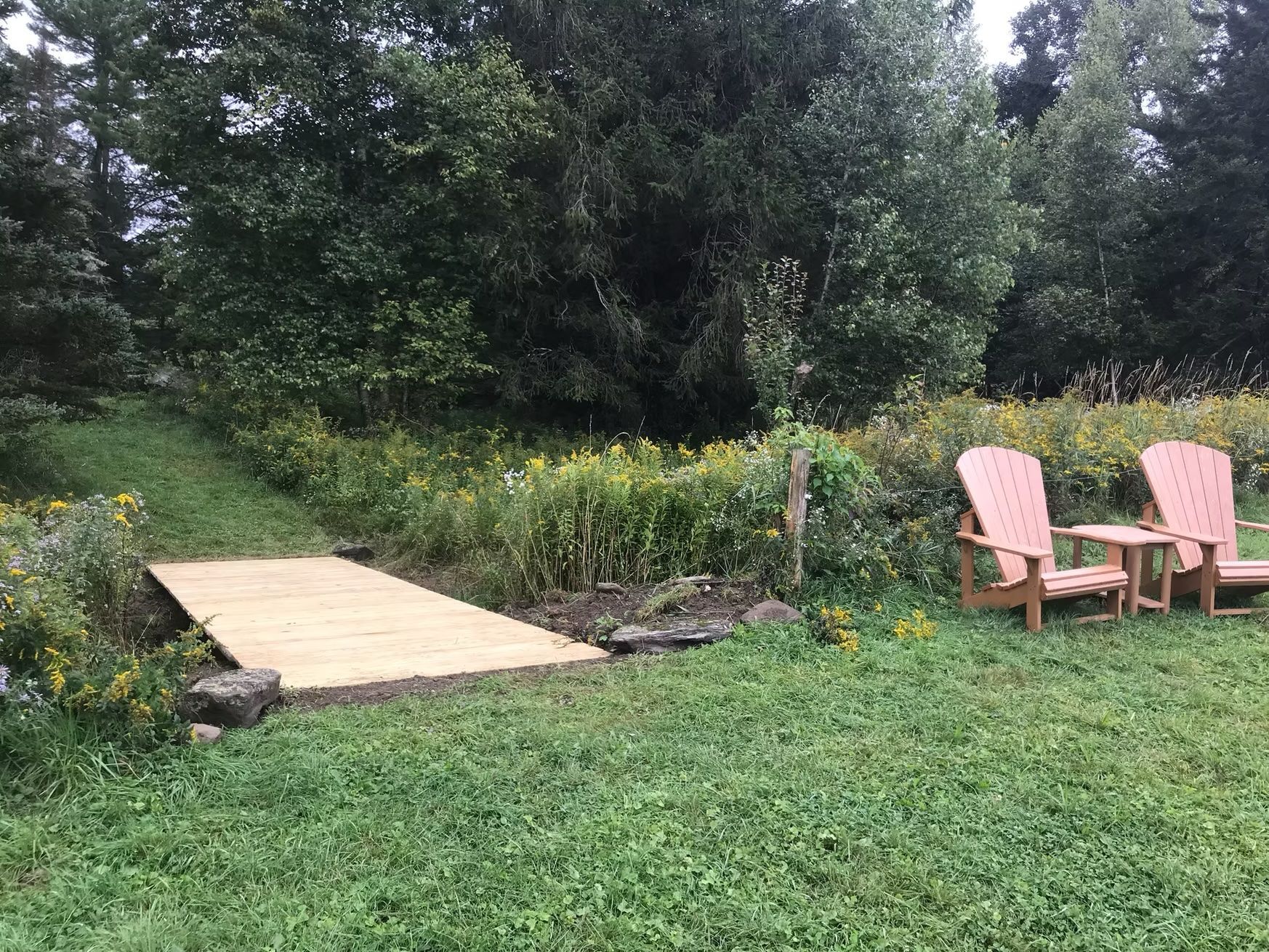 A couple of chairs sitting on top of a lush green field next to a wooden bridge.