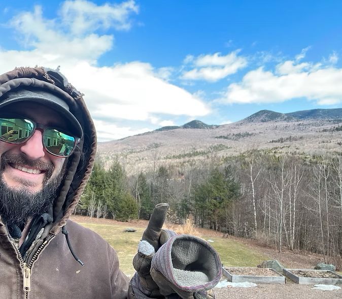 A man with a beard wearing sunglasses and a hood is holding a pipe in his hand.
