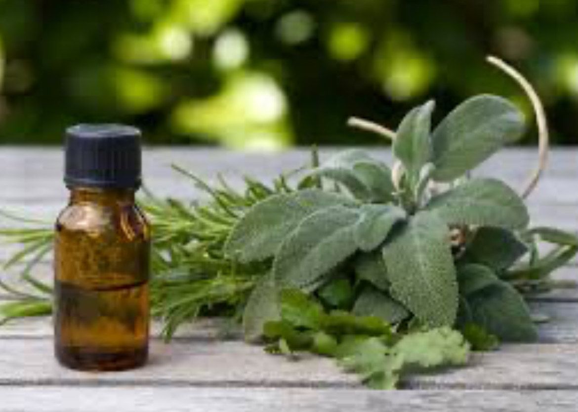 A bottle of essential oil next to a bunch of herbs on a wooden table.