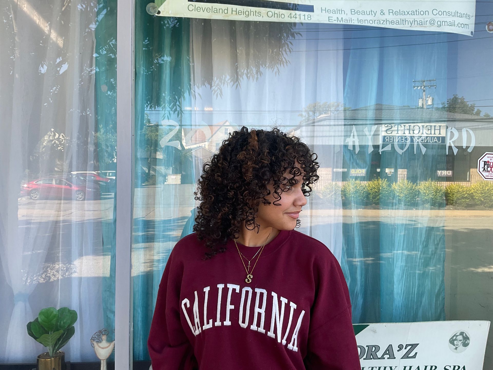 A woman wearing a california sweatshirt is standing in front of a window.