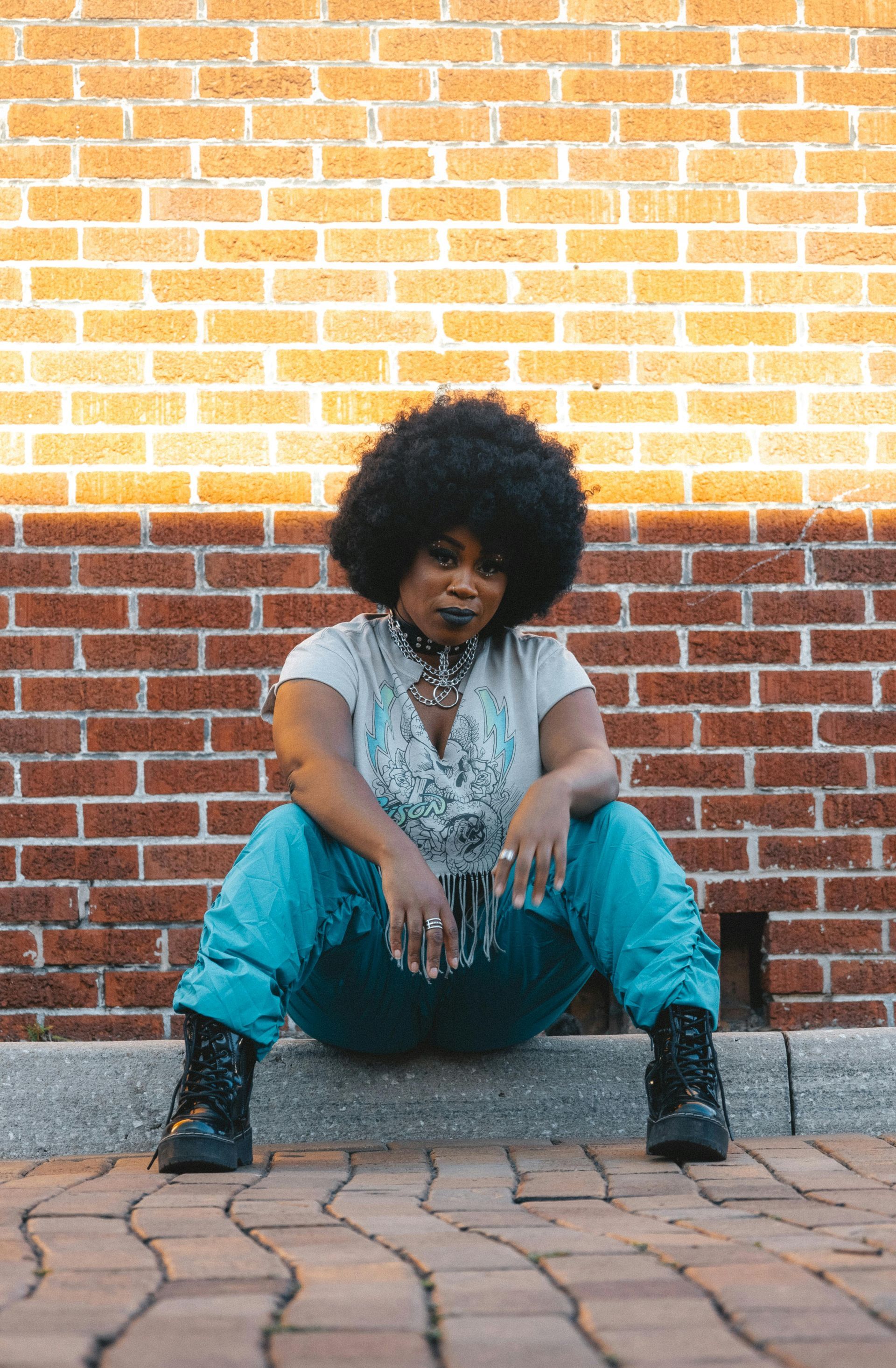 A woman is sitting on a curb in front of a brick wall.