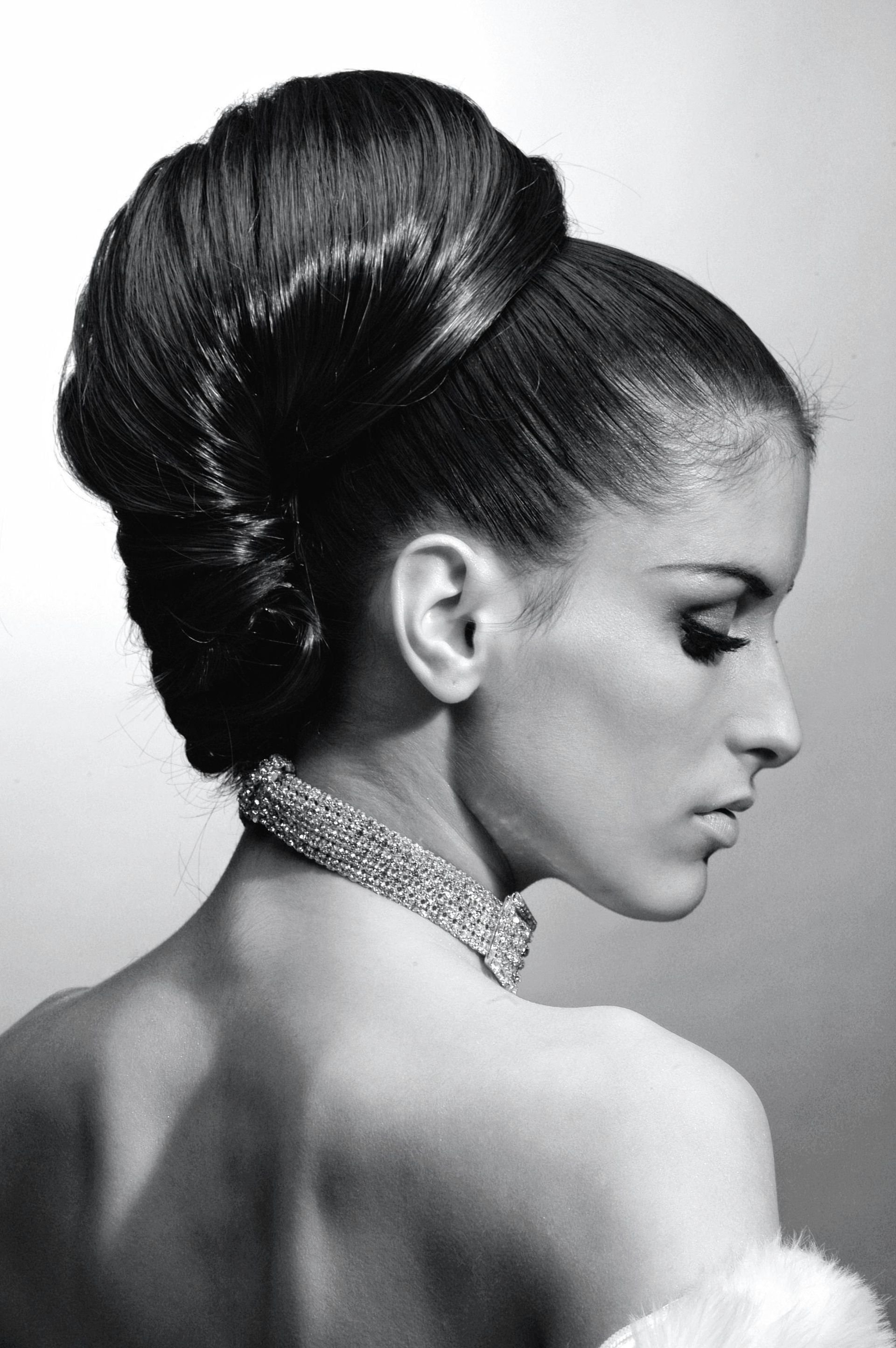 A black and white photo of a woman wearing a necklace and a bun.