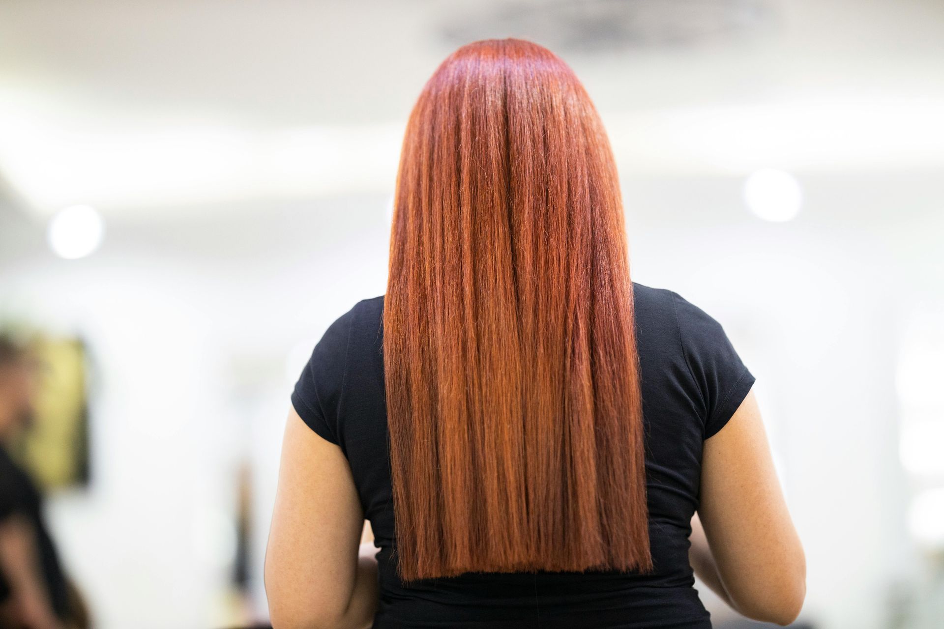 A woman with long red hair is standing in a salon.