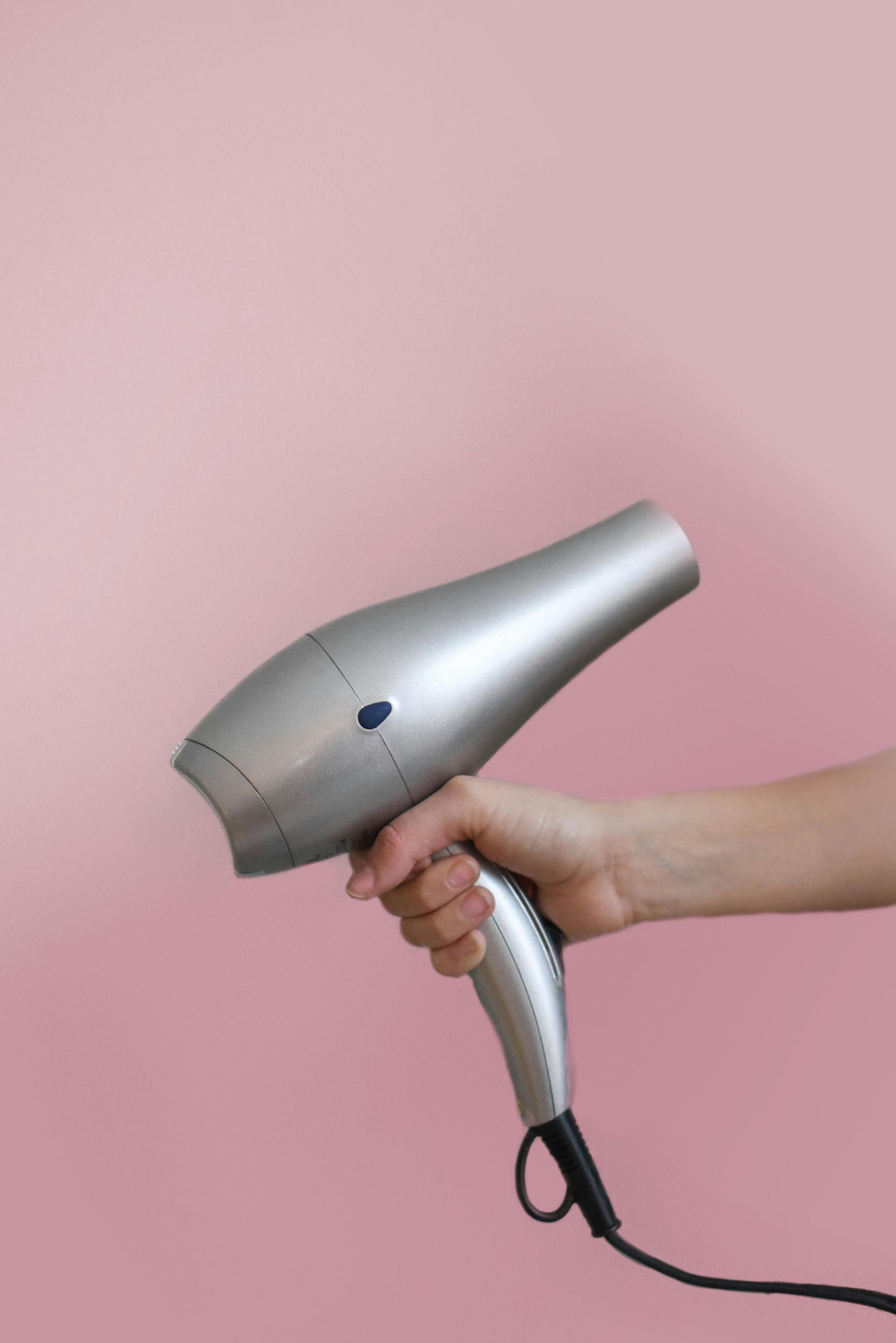A person is holding a hair dryer in their hand against a pink background.