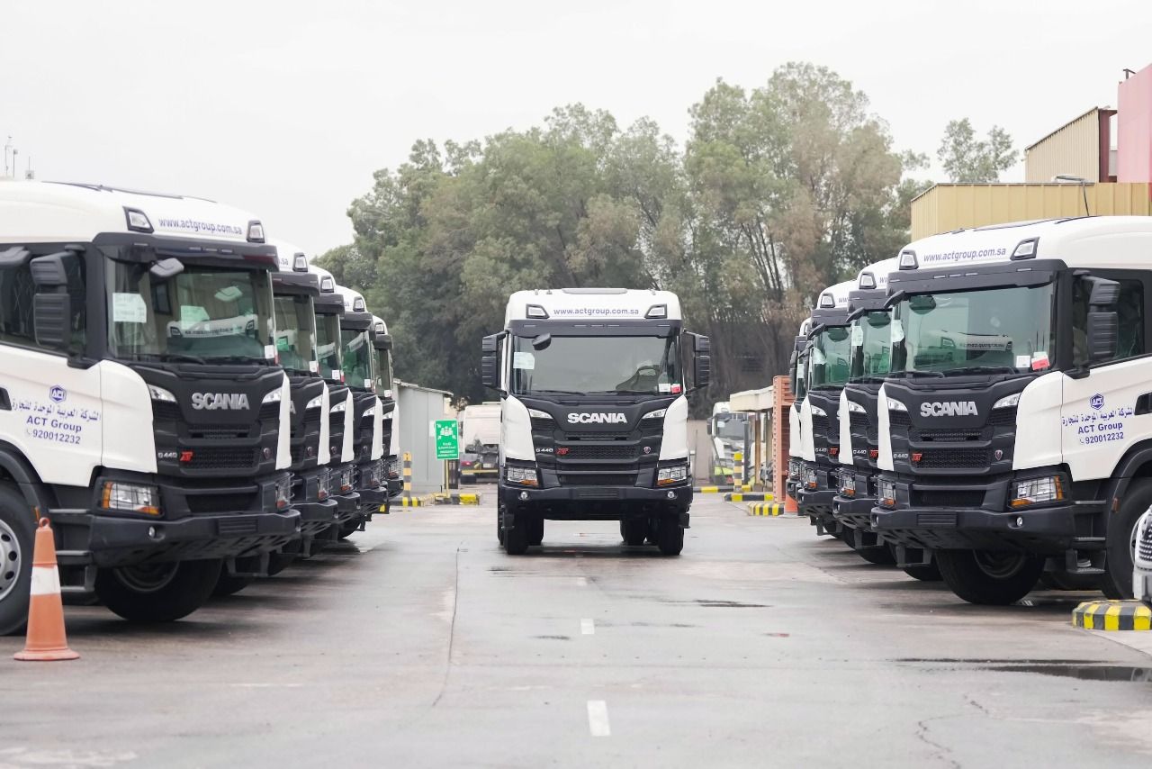 A line of white Scania trucks parked on a concrete lot, with a single truck centered.