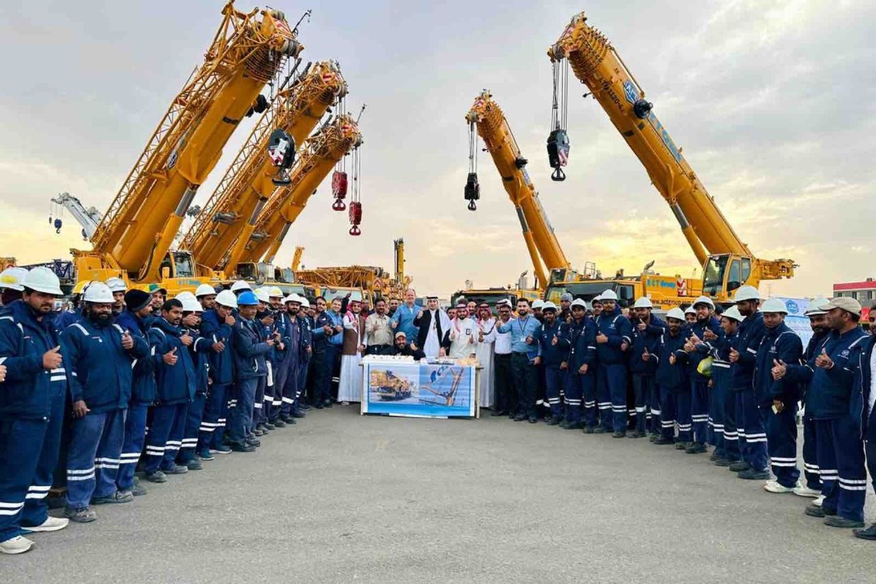 Group of workers in blue uniforms with yellow cranes, standing around a table outdoors.