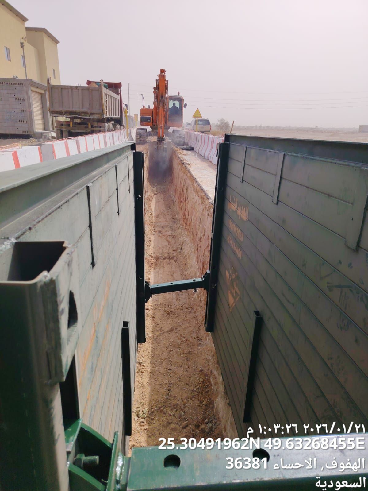 Construction worker in blue hard hat and orange vest, operating machinery near a building.