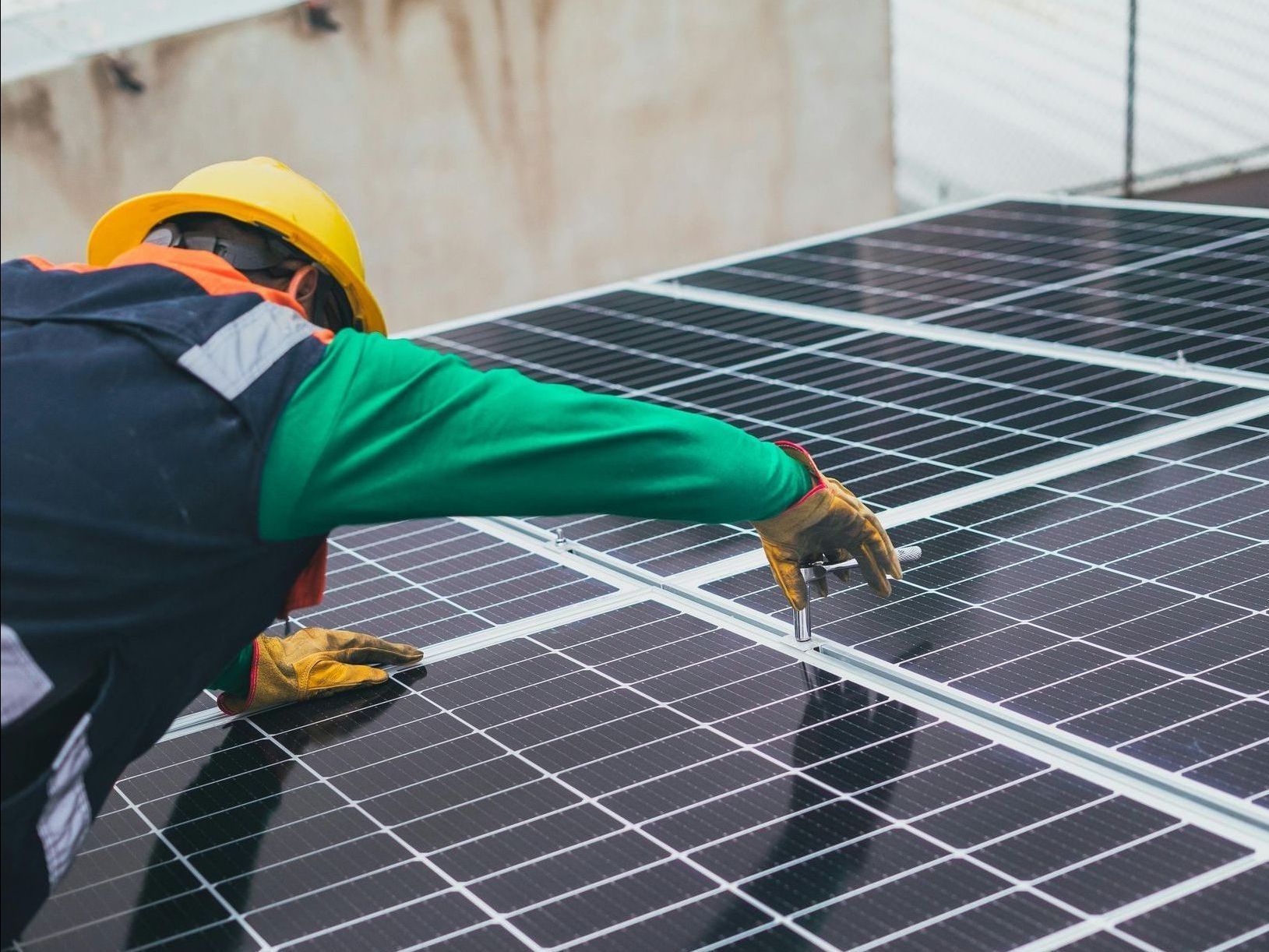 Person in safety gear installing solar panels on a rooftop.